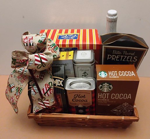 Gift basket with hot cocoa, coffee cake, pretzels, and other snacks on a neutral background