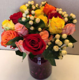 A vibrant Christmas flower bouquet featuring a variety of fresh flowers, including roses, carnations, and greenery, arranged in a purple vase.
