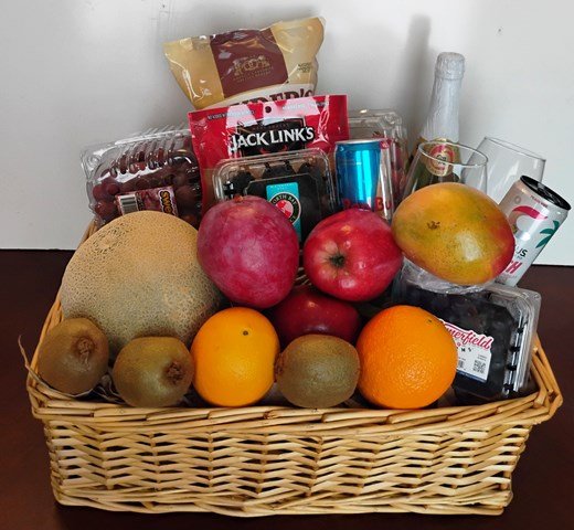Fruit basket with various fruits and snacks on a wooden surface. Sports drinks and baked pastry.