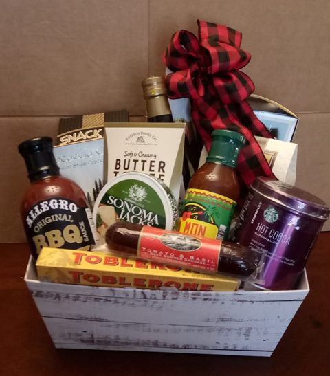 Gift basket with barbecue sauce, crackers, chocolate, and hot cocoa, topped with a red-and-black plaid bow