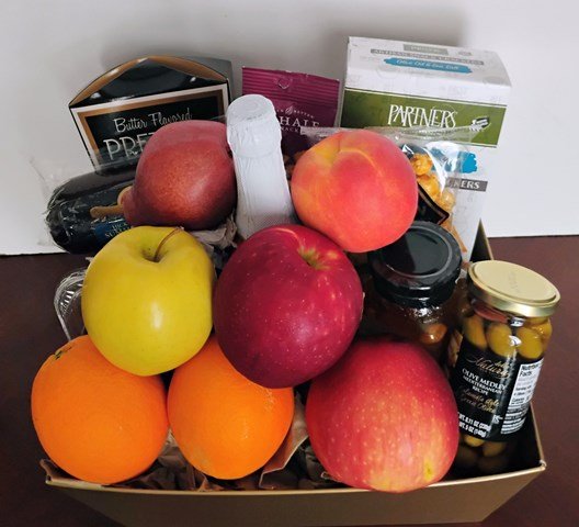 Fruit and snack gift tray with red and green apples, oranges, pretzels, crackers, and garlic-stuffed olives
