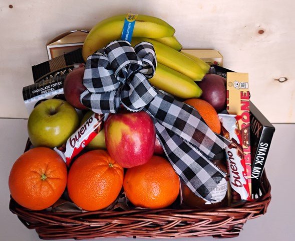 Basket filled with fresh fruit and packaged snacks, tied with a black-and-white ribbon. Oranges and apples, 
