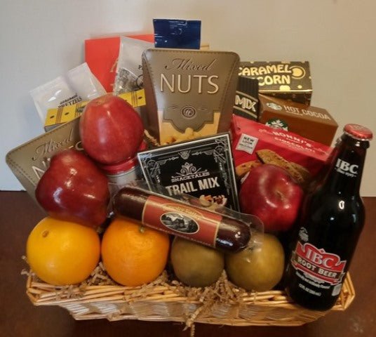 Wicker fruit and snack tray with apples, oranges, pears, mixed nuts, trail mix, sausage, and root beer