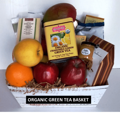 White gift box with chamomile lemon green tea, red apples, an orange, a mango, cheese, and crackers