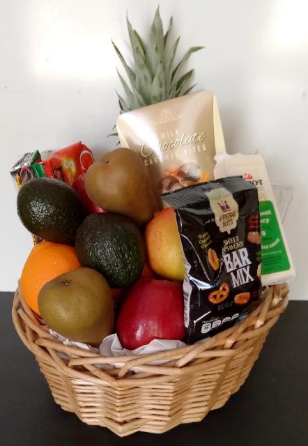 Wicker fruit and snack basket with pineapple, avocados, apples, pears, an orange, chocolates, and bar mix