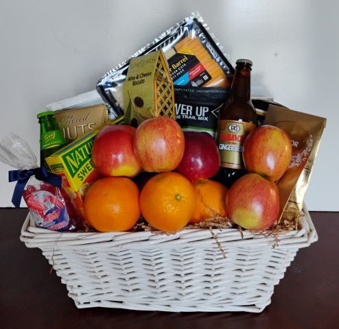 White wicker gift basket with apples, oranges, cheese, crackers, mixed nuts, trail mix and ginger beer
